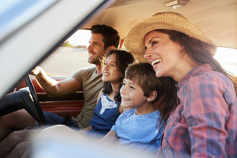 About Our Agency - View of Cheerful Family with Two Kids Sitting in a Car During a Summer Road Trip to the Countryside