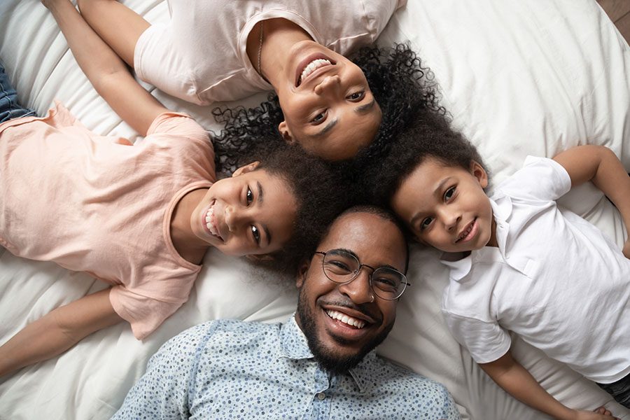 Personal Insurance - Portrait of Happy Family with Two Kids Laying on the Bed Having Fun Playing Together at Home